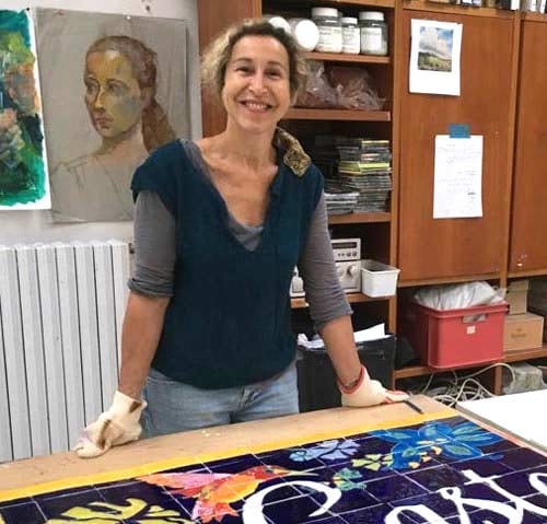 Laurence Brecher dans son atelier, devant un grand panneau de carreaux qui sort de l’émaillage