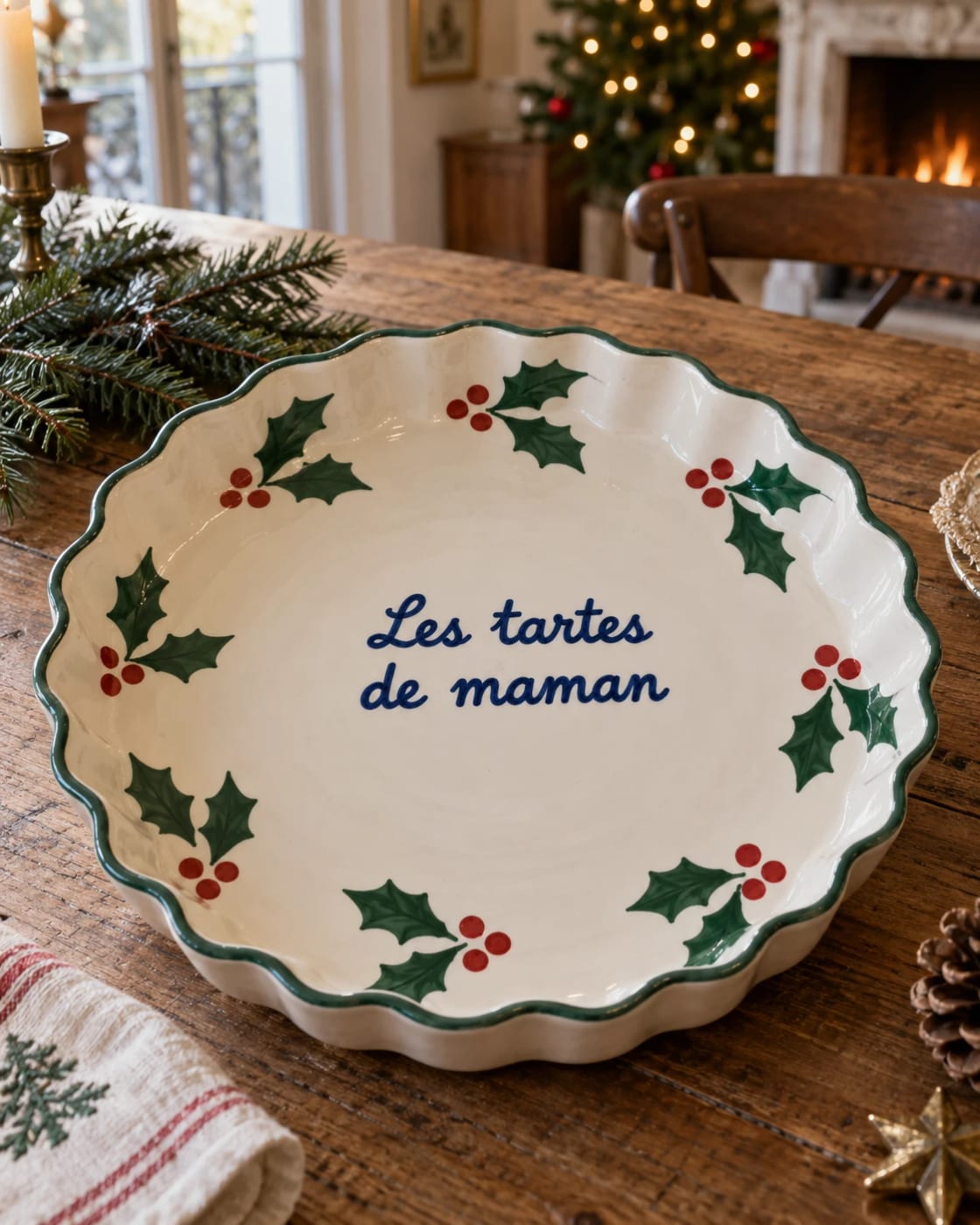 Une idée de plat à tarte en céramique à bord festonné, « Les tartes de maman » au centre et couronne de houx peinte à la main, sur une table de Noël